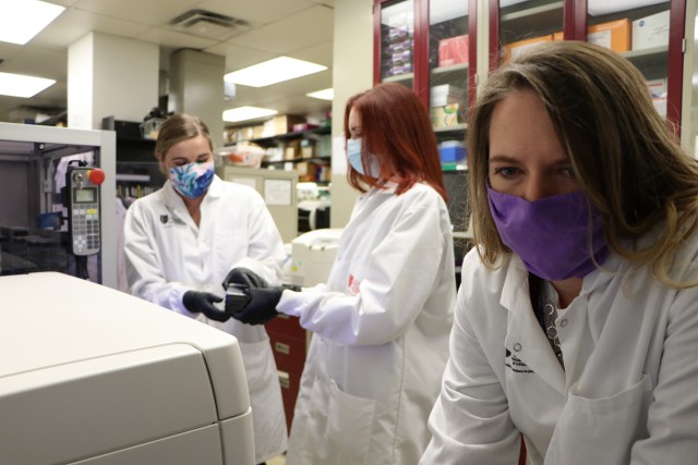 Army researchers Laura Prugar (blue mask), Kathleen Huie (print mask) and Nicole Josleyn (purple mask) use a microneutralization assay and a high-throughput fluorescent imaging system to determine levels of neutralizing antibody to SARS-CoV-2 in convalescent patients. 