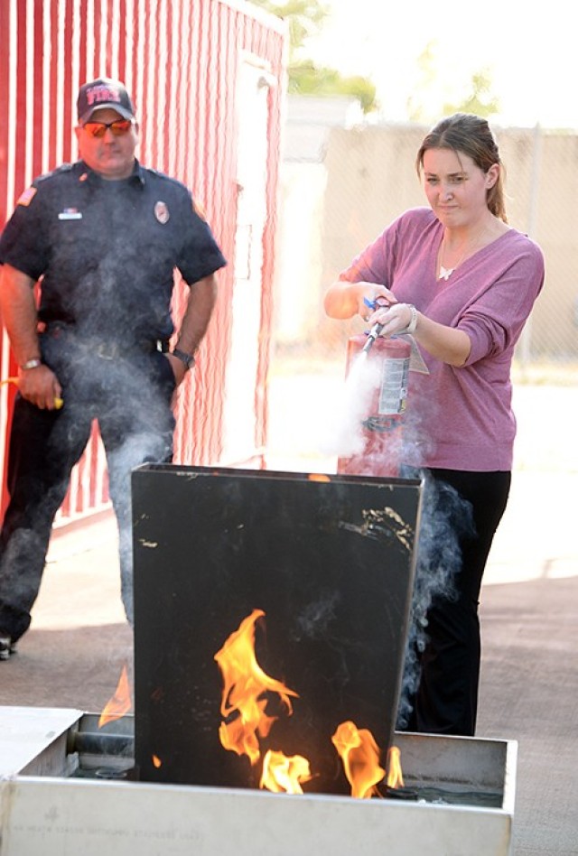 Fire Inspector Antonio Masisak controls the fire extinguisher trainer as Katie Peterson, Fort Leavenworth Lamp reporter, practices using a fire extinguisher, keeping in mind the acronym PASS (pull the pin, aim at the base of the fire, squeeze the...
