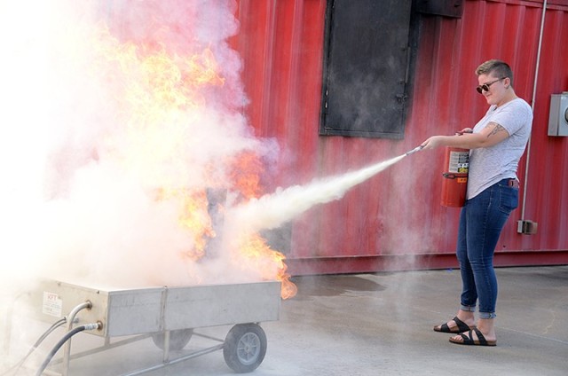 Annika Kinder, Fort Leavenworth Public Affairs intern and senior at Park University, practices putting out a fire with the Fort Leavenworth Fire and Emergency Services' fire extinguisher trainer, keeping in mind the acronym PASS (pull the pin, aim...