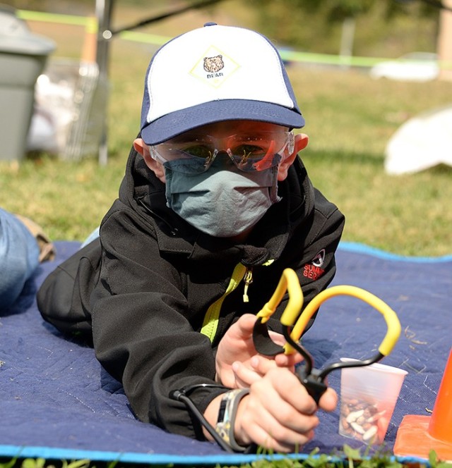 With a cup full of ammunition — dry beans — and a slingshot properly placed around his wrist, 8-year-old Clayton Tucker waits for the signal so he can take aim at the targets — a row of hanging pie tins — during the Cub Scout Pack 1...