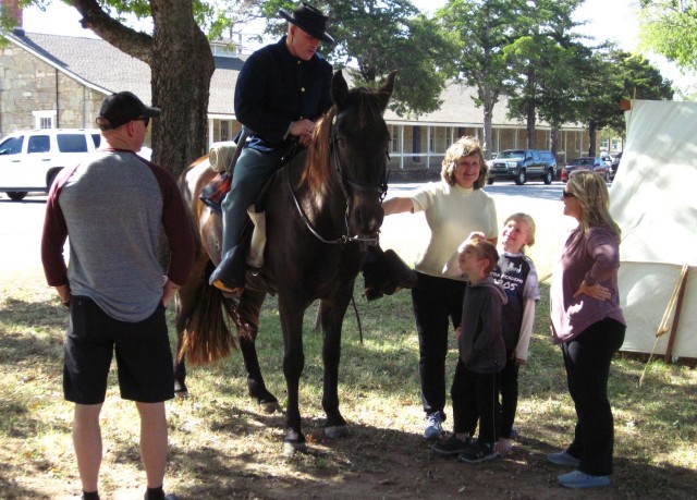 From left, Sgt. 1st Class Anthony Hantaq, Debbie Burroughs, Andrew Atkinson, 5, Abigail Atkinson, 8, and Jennifer Atkinson pepper Brent Harty, astride his horse Jeffers, with questions about his mid-19th century frontier life as a cavalryman. It was part of the Frontier Army Days living history Oct. 17, 2020, at the Old Post Quadrangle on Fort Sill, Oklahoma. 
                      