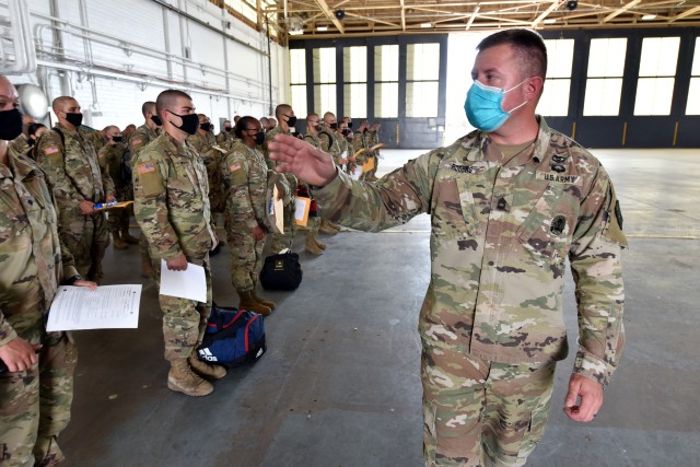 Sgt. 1st Class Garrett Rogers, Movement Non-commissioned Officer in Charge for the 32nd Medical Brigade, directs Soldiers standing in formation inside a hangar at Kelly Field during a layover as they travelled from Fort Jackson to Fort Huachuca. These Soldiers were on a chartered flight along with Soldiers that also departed Fort Jackson to begin training at the U.S. Army Medical Center of Excellence.