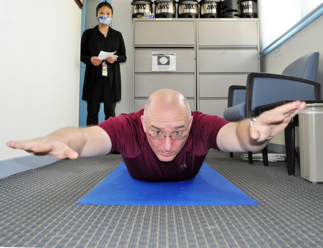 Stephen Harmon, a health promotion technician for the Camp Zama Army Wellness Center, demonstrates a “Superman” push-up at the center, Camp Zama, Japan, Nov. 3. Shannon Vo, a health educator at the center, looks on. The exercise is one example...