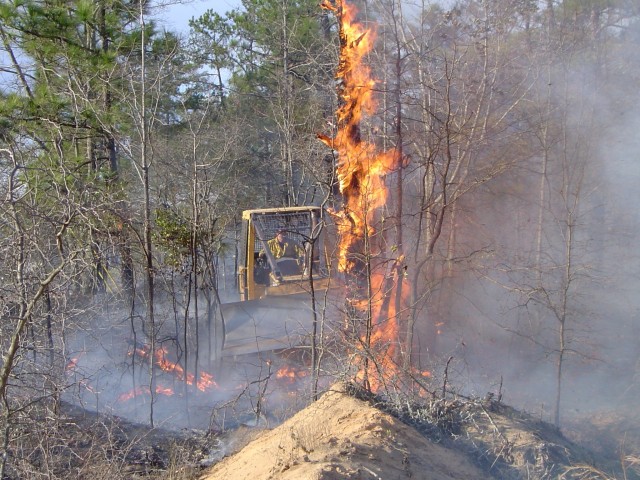 FORT BENNING, Ga. – In a March 2004 photo, a member of a Fort Benning prescribed burn crew uses a bulldozer to move a burning dead tree to where it can&#39;t spread fire outside the space within which the crew wants to burn. Each year from December through May Fort Benning conducts expertly controlled burns of deadwood and other debris on the forest floor, because it limits interruption of military training and helps Fort Benning&#39;s plant and animal life. Before such burns are scheduled, officials here carefully study weather data, including forecasts as to wind direction, and avoid burning at times or places that might lead to smoke carrying to local homes, hospitals, schools, businesses, roadways, or airports.

(U.S. Army photo courtesy of Directorate of Public Works, U.S. Army Garrison Fort Benning)