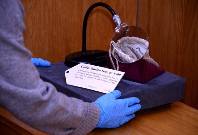 Museum Technician Fayelee Overman positions a circa 1900 coffee ration bag, with a magnifying glass to help see the remaining coffee grounds in the bottom of the bag, while installing an exhibit on "Coffee in the Army" Nov. 20 at the Frontier Army...