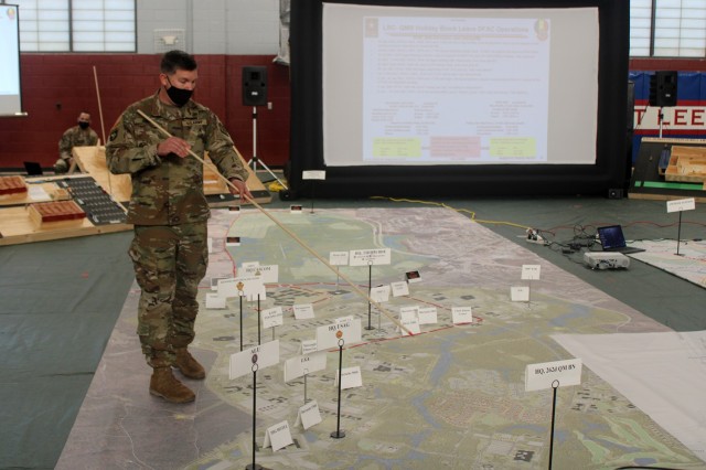 Sgt. 1st Class Vernon Inman from the CASCOM G-3 (Training) office, points at a location on a massive Fort Lee floor map that was the centerpiece for a holiday block leave rehearsal of concept drill Nov. 18 in MacLaughlin Fitness Center. Well-planned and synchronized operations are vital to the annual operation that involves pre-departure safety and proper conduct training for several thousand troops, clearing and securing barracks rooms, staging for  movement to transportation hubs, receiving service members upon their return to Fort Lee, and much more. HBL operations will begin in mid-December.