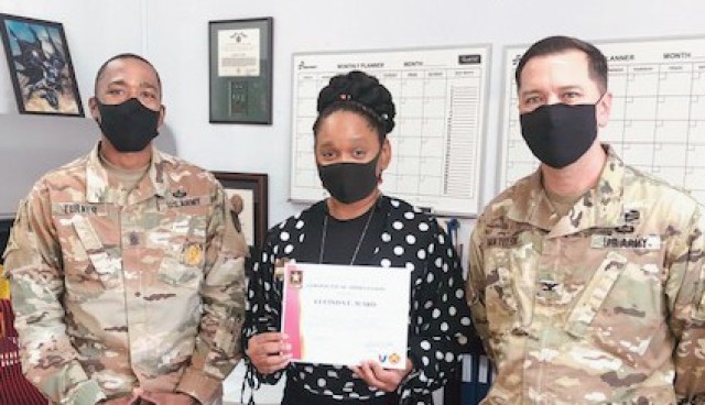 Col. Thomas Matelski, right, commander of U.S. Army Garrison Japan, and Command Sgt. Maj. Justin Turner, the garrison’s incoming CSM, recognize Lucinda Ward at Camp Zama, Japan, Dec. 11, for putting together a Japanese birthday gift for Victor...