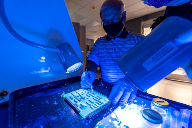 William Rumble, electronics technician, performs the post-repair conformal coating inspection and touch-up process on a Volcano CCA. Acrylated polyurethane conformal coating applied to each CCA contains a tracer that fluoresces brightly when...