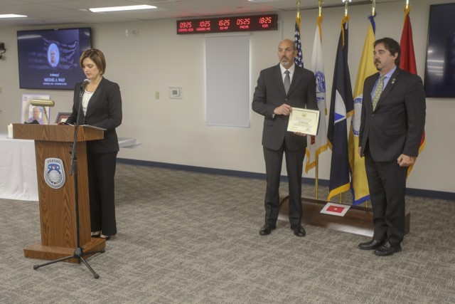 Terra Good, left, the Security Assistance Liaison Office program manager, and narrator for the awards citation, reads a letter from Pennsylvania Senator Patrick Toomey, while James Sharkey, chief of case development, presents the award to Michael Casciaro, the assistant chief of staff and senior USASAC representative in New Cumberland, Pa. Casciaro accepted the awards on behalf of Walp’s family, on Dec 10 in New Cumberland.