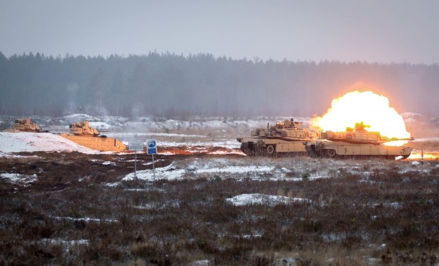 Bradley Fighting Vehicles are bathed in a red and orange glow from ignited gasses as an M1 Abrams tank’s main gun fires Dec. 22, 2020, at the Pabrade Training Area, Lithuania. The vehicles, assigned to 2nd Battalion, 8th Cavalry Regiment, 1st...