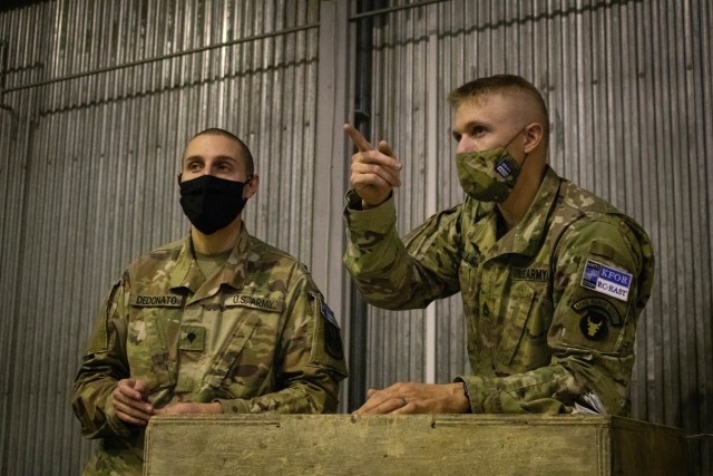Sgt. 1st Class Joshua Wells, mortuary affairs noncommissioned officer in charge, Regional Command-East, Kosovo Force, assists Spc. Matt Dedonato, an avionics mechanic with 3rd Battalion, 238th General Support Aviation Battalion, Delaware Army...