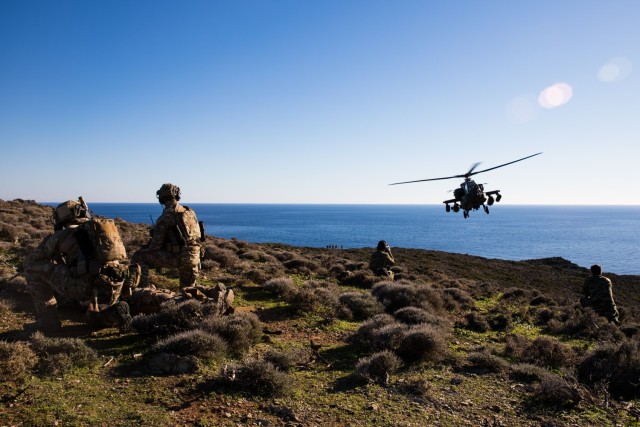 A U.S. Army AH-64E attack helicopter assigned to 1st Battalion, 101st Combat Aviation Brigade, 101st Airborne Division (Air Assault) flies over Hellenic special operations forces soldiers on Velopoula Island in the Aegean Sea in Greece, Jan. 14,...