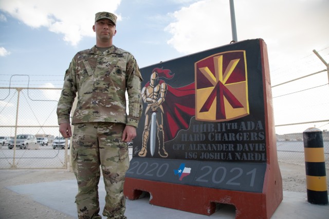 Sgt. 1st Class Brandon Brouillet assigned to Headquarters and Headquarters Battery, 11th Air Defense Artillery Brigade, poses in front of his designed unit T-Barrier, Jan. 11, 2021, at Al Udeid Air Base. (U.S. Army photo by Staff Sgt. Mariah Jones)