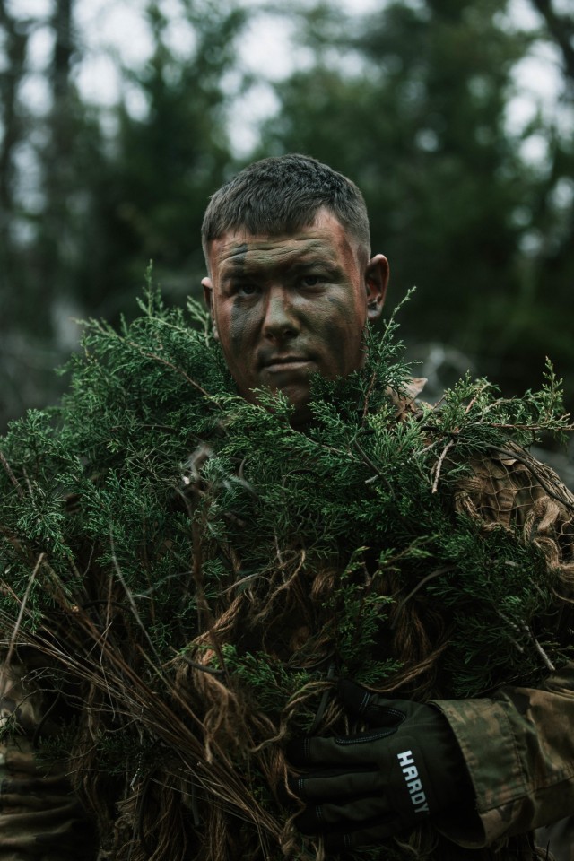 Spc. Jarrod Thomas, a Sniper with 1st Battalion, 12th Cavalry Regiment, 3rd Armored Brigade Combat Team, 1st Cavalry Division, looks up to the camera after donning his “vegged-up” uniform during a movement, cover, and concealment training exercise, Fort Hood, Texas, Jan. 20, 2021. (U.S. Army photo by Sgt. Calab Franklin)