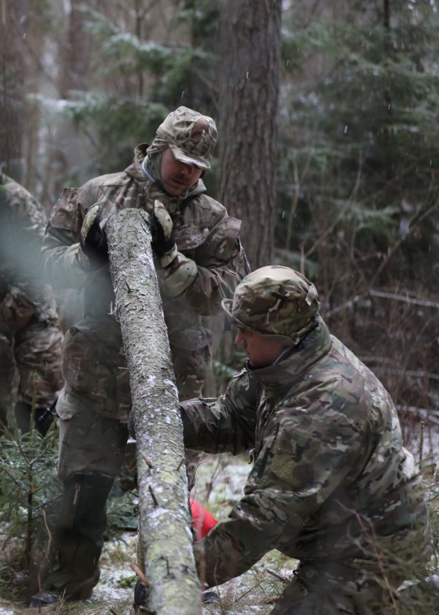 Instructor from the U.K. Land Warfare Center teaches  U.K. Troops from NATO enhanced Forward Presence Battle Group Poland teaches British Soldiers how to set a trap for game during a cold weather operator's course Dec. 11, 2020  at Bemowo Piskie...
