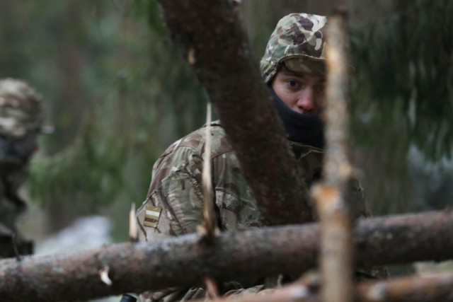 British Trooper from enhanced Forward Presence Battle Group-Poland peers through the limbs in the foundation of an overnight shelter during a cold weather operator's course Dec. 11, 2020 at Bemowo Piskie Training Area, Poland. (U.S. Army photo by...