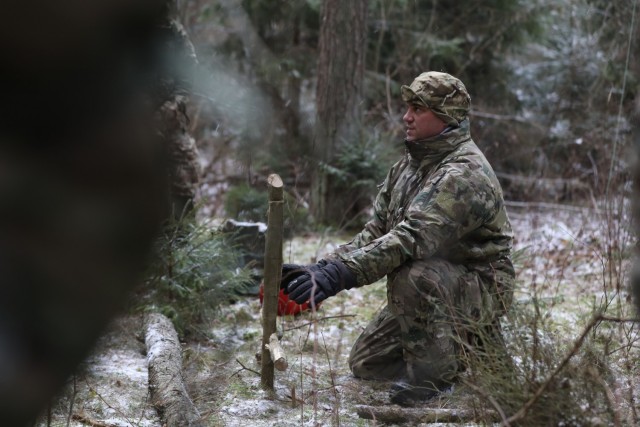 Instructor from the U.K. Land Warfare Center teaches British Troops from NATO enhanced Forward Presence Battle Group Poland how to make a snare from items in the environment and theirr field kit during a cold weather operator's course Dec. 11,...