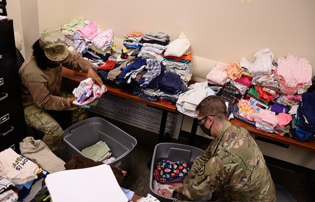 Pvt. Monique Mason, 291st Military Police Company, 40th Military Police Battalion (Detention), and Spc. Joshua Solano, 256th MP Company, 40th, pack pre-sorted children's clothing into bins to transfer the donations from a temporary collection site...