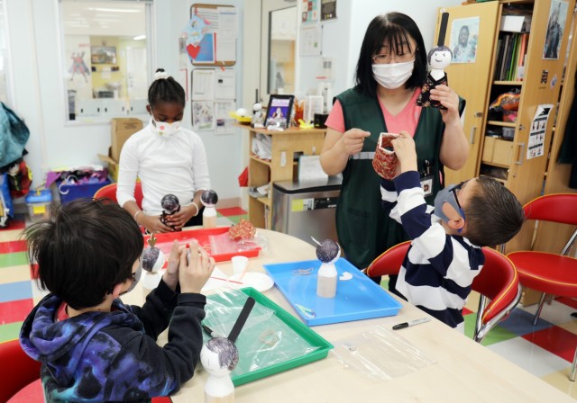 Marino Nakanowatari, right, a caregiver in the art room at the School Age Center, helps students during a virtual class on how to make Japanese “Hinamatsuri” dolls, Sagamihara Family Housing Area, Japan, Feb. 9.