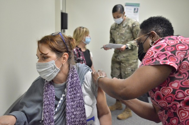 Kesha Ladd, Fort Campbell High School teacher, foreground, receives a COVID-19 vaccination, Feb. 12, from Patsey Simmons, licensed practical nurse, while Kimberly Butts, FCHS guidance counselor, reviews information with Sgt. Tametra Jalomo, medic...