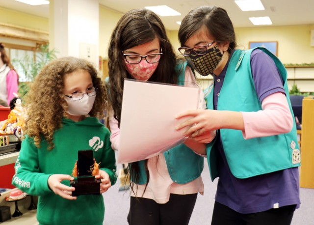 At center and right, Layla and Lilly de Castro, both 10, and both members of Junior Girl Scout Troop 67, work with Cailyn Nelson, left, 8, a member of Brownie Troop 11, while setting up a “Hinamatsuri” display at the Camp Zama Library, Camp...