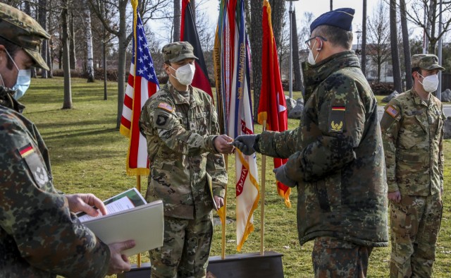 Brig. Gen. Thomas Hambach, Commander Landeskommando Bayern, presents Sgt. Patrick Carter, assigned to Bravo Company, 6th General Support Aviation Battalion, 101st Combat Aviation Brigade, with the Commanders Golden Coin, during an awards ceremony recognizing Carter's air crew for their efforts, Grafenwoehr, Germany, Feb. 18, 2021. Brig. Gen. Christopher Norrie, Commander, 7th Army Training Command, and Brig. Gen. Thomas Hambach, were both present at the award ceremony to thank the crew for their heroic actions.