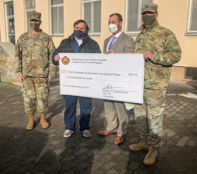Garrison Commander Col. Mario Washington, accompanied by Command Sgt. Maj. Christopher Truchon and Scott Mowry, deputy to the garrison commander, issue the $500 award and certificate of recognition to David Mills, clerk for Value Added Tax...