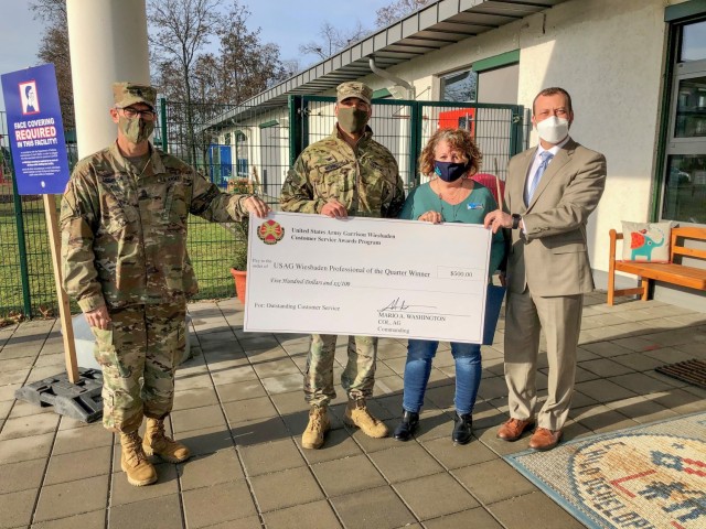 Garrison Commander Col. Mario Washington, accompanied by Command Sgt. Maj. Christopher Truchon and Scott Mowry, deputy to the garrison commander, issue the $500 award and certificate of recognition to Susan Hutchings, facility director Family and...