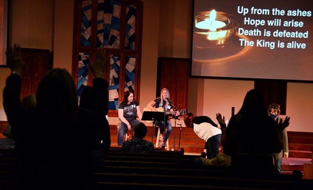 Caitlyn Mair, praise and worship leader for Protestant Women of the Chapel, and singer Kayla Atkins lead PWOC members in singing "Raise a Hallelujah" as worship service participants place their burdens, written on index cards, on the alter March 9...