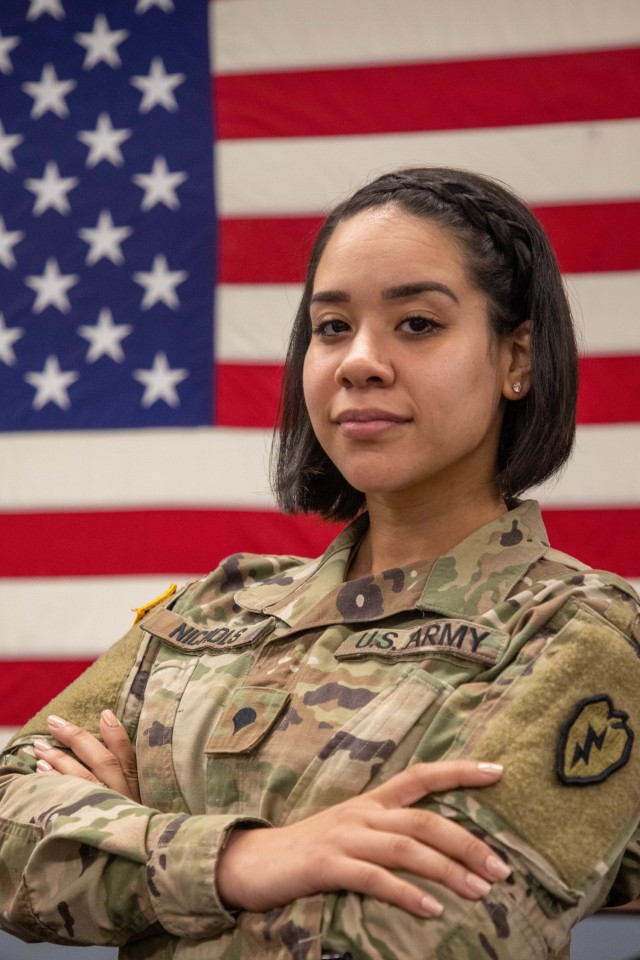 Spc. Kiala Nichols, an Aviation Operation Specialist (15P), assigned to 25th Combat Aviation Brigade, 25th Infantry Division at Wheeler Army Airfield, Hawaii, poses for a photo in front of an American flag. Nichols is wearing earrings and nail polish in her combat uniform while still maintaining professionalism after the announcement of changes to the Army Grooming Standards AR 670- 1 on Feb. 24, 2020. (U.S. Army photo by Sgt. Sarah D. Sangster)