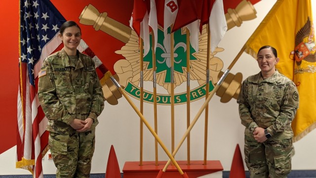 U.S. Army Sgt. Jennifer Ponce and Sgt. Kelley Chilauskas stand in front of the unit colors in Rose Barracks, Germany, Mar. 15, 2021. They shared their stories in support of Women's History Month. (U.S. Army photo by 1st Lt. Anastasia Harmon)