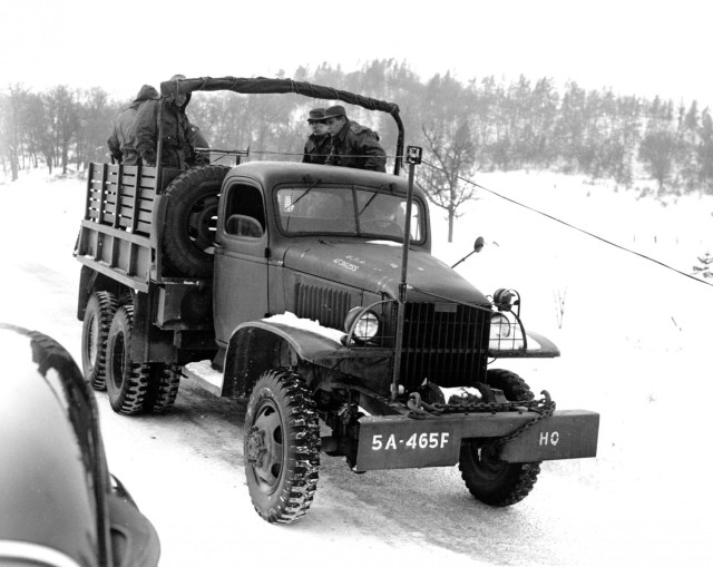 Soldiers demonstrate use of a device attached to 2.5 ton 6x6 truck March 19, 1951, used for picking up W 110 B wire in open terrain at Camp McCoy, Wis.  This device picks up the wire from the side of the road or in open country by lifting it off of the ground through the tension of a power-driven winch on the back of the vehicle. Wire is picked up over the front of the truck, eliminating a loop in the wire  and a wire crew on the ground, giving it a practiced pick-up speed of 10 to 12 miles per hour with an experienced crew.  The device consists of two vertical and horizontal rollers mounted on a rod over the front bumper, and two horizontal rollers in the rear of the cab, enabling the wire to clear the cab.  The pick-up accomplished by a power-driven winch with a clutch.  The device was developed by Sgt. Walter Wehr of Minor, N.D., now with the 465th Field Artillery battalion, Camp McCoy, Wis.  (Historical photo)