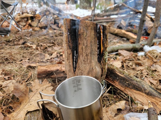 A coffee mug warms over a fire as students in Cold-Weather Operations Course class 21-05 conduct field training with improvised shelters March 16, 2021, at a training area at Fort McCoy, Wis. CWOC students are trained on a variety of cold-weather...