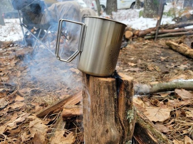 A coffee mug warms over a fire as students in Cold-Weather Operations Course class 21-05 conduct field training with improvised shelters March 16, 2021, at a training area at Fort McCoy, Wis. CWOC students are trained on a variety of cold-weather...