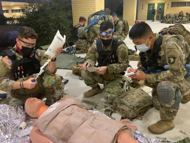 Sgt. Carter McCall (left) simulates point of injury care while CPT Alexander Goncalves provides a patient update to the Tactical Combat Medical Care, or TCMC, course student team lead during TCMC’s trauma lane scenarios on Joint Base San Antonio-Fort Sam Houston, Texas, March 18, 2021.