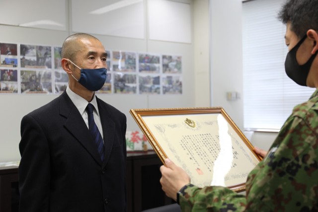 Yoshihiro Isono, left, assigned to the U.S. Army Garrison Japan Directorate of Plans, Training, Mobilization and Security, receives a certificate of appreciation from Col. Kazuya Ono, commander of the JGSDF’s 4th Engineer Group and JGSDF Camp...