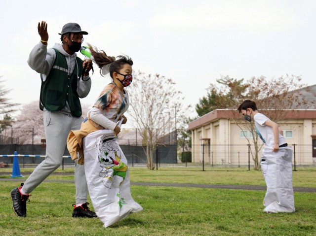 Lara Shimabuku, a second-grader, participates in the “SAC Race” during the 2021 School Age Center Olympics at Sagamihara Family Housing Area, Japan, April 1. Alex Jones, a staff member, cheers her on, and Max Matthews, right, a second-grader,...