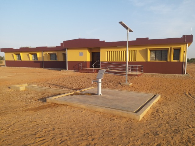 A recently completed health clinic, with a water well hand pump on a concrete pad and a solar powered light pole seen in the foreground, is seen here in the remote village of Money in Benin in Africa. The clinic and various associated facilities...