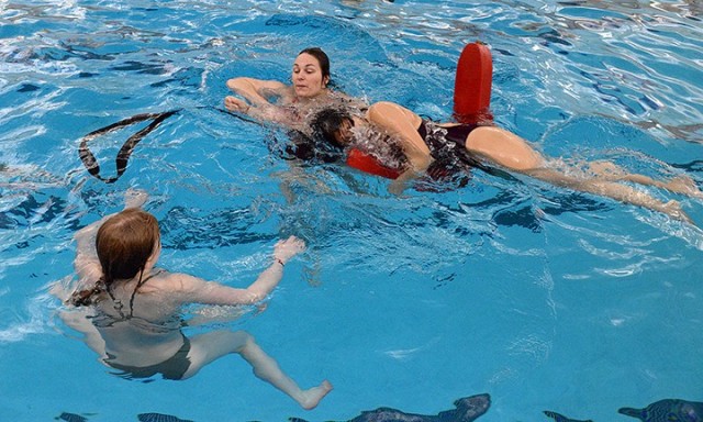 Kate Brooks watches lifeguard training instructor Thula Stenerson show her how to use momentum to pull Ashley Morgan onto a lifeguard rescue tube during lifeguard training April 3 at Harney Pool. Lifeguard training students took turns practicing...