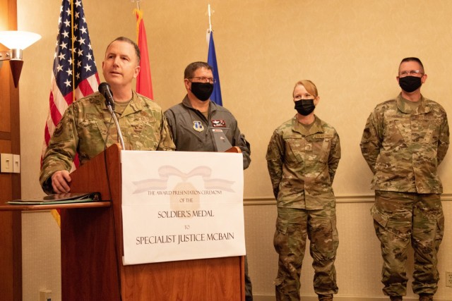 Brig. Gen. David May (far left), deputy adjutant general of the Wisconsin Air National Guard, presents his remarks during the presentation ceremony of the Soldier’s Medal to Spc. Justice McBain, April 11, 2021, at Milwaukee, Wisconsin. (U.S. Army Reserve photo by Maj. Jeku Arce)