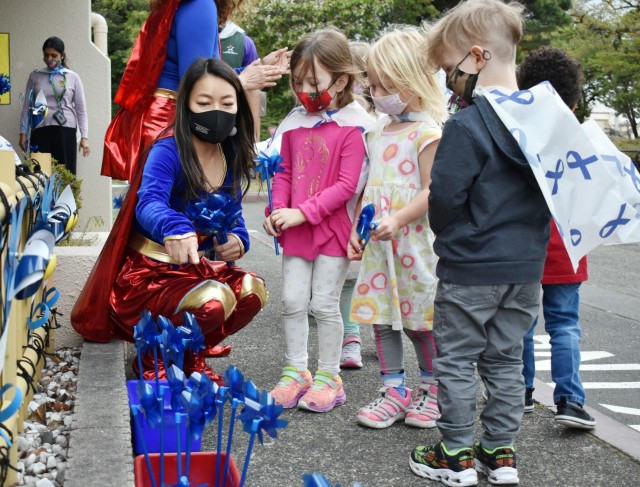 Sari Sugai, Exceptional Family Member Program manager for Army Community Service, helps, from left, Rose Withington, 4; Claire Herald, 3; and Torin Litton, 3, plant pinwheels at the Child Development Center at the Sagamihara Family Housing Area,...