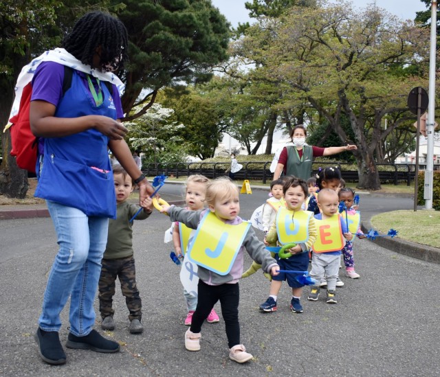 Tiara Harris, left, and Shiela Imagawa, right, Child Development Center staff, lead toddlers on a superhero parade at the Child Development Center at the Sagamihara Family Housing Area, Japan, April 9. Camp Zama Family and Morale, Welfare and...