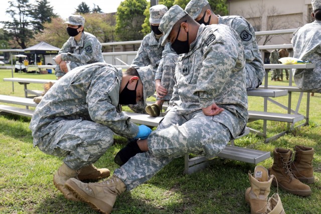 Cadet Command Sgt. Maj. Michael Nonaka, left, treats a blister on the foot of Cadet Lt. Col. Jayson Loiselle, commander of the “Trojan Battalion,” after a nearly 3-mile road march during the Zama Middle High School Junior Reserve Officers’...