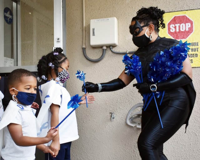 Lucinda Ward, Army Community Service specialist, hands a pinwheel to DeStani Muex-Mabon, 5, before a superhero parade at the Child Development Center at the Sagamihara Family Housing Area, Japan, April 9. Chance Garrett, 3, stands next to them....