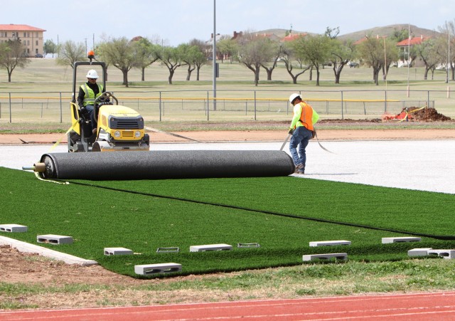 Adam Garley of Pro Turf Incorporated of Haslet, Texas, rolls out a 15-foot by 100-foot section of artificial turf April 9, 2021, at Prichard Field. Once all turf was placed, Pro Turf workers glued the sections together then nailed the perimeter...