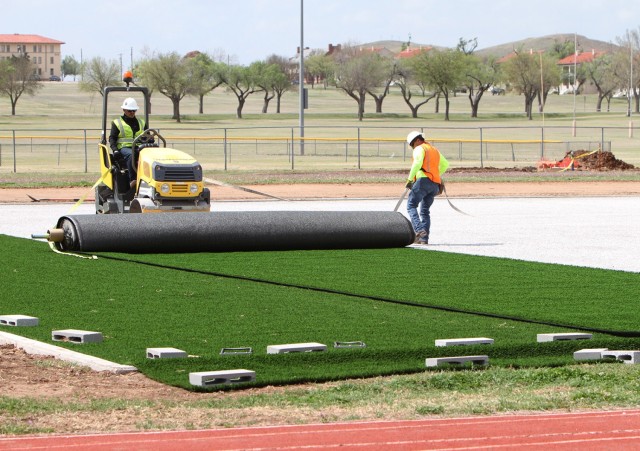 Adam Garley of Pro Turf Incorporated of Haslet, Texas, rolls out a 15-foot by 100-foot section of artificial turf April 9, 2021, at Prichard Field. Once all turf was placed, Pro Turf workers glued the sections together then nailed the perimeter down to the fine gravel base underneath.