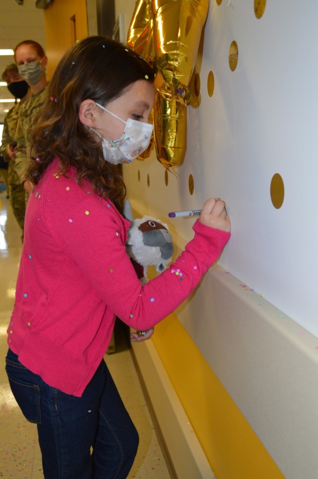 Seven-year-old Sailor Parker writes her name on a wall sticker after she rang the bell in the Brooke Army Medical Center Pediatric Hematology/Oncology Clinic April 1, 2021, signifying she won her battle against Acute Lymphocytic Leukemia. Acute Lymphocytic Leukemia is the most common type of cancer in children and adolescents, but only happens at a rate of 34 per million in those who are under 20 years of age. (U.S. Army photo by Lori Newman)