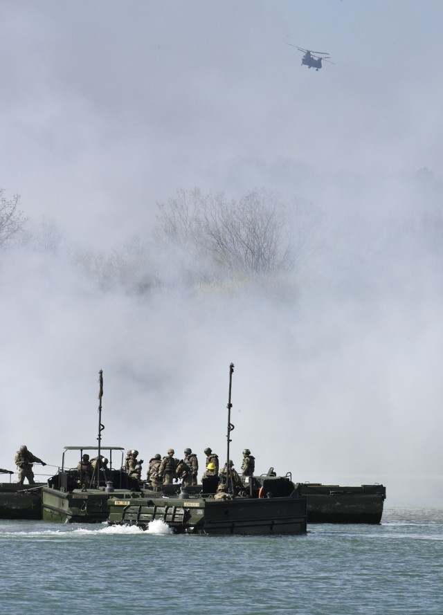 A CH-47 Chinook helicopter circles overhead as bridge crewmember trainees from Company A, 35th Engineer Battalion, prepare to build float bridges on the lake at TA 250 while smoke obscures their view during the FTX.