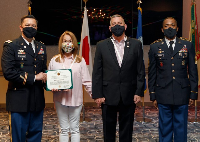 U.S. Army Garrison Japan commander Col. Thomas Matelski (left) and Command Sgt. Major Justin Turner (right) present Janet Niederriter with the Public Service Commendation Medal during J. Steve Niederriter’s retirement ceremony April 16, 2021, at...