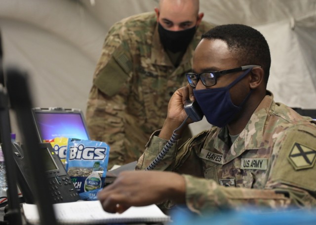 Alabama National Guard Spc. Anthony Hayes, working communications and information systems for the 1st Theater Sustainment Command's expeditionary command post validation exercise at Camp Arifjan, Kuwait, calls to follow up on a help ticket April 12, 2021, alongside Alabama National Guard Spc. Timothy Decker. The guardsmen, both deployed to Kuwait with the 115th Expeditionary Signal Battalion, manned the ECP's Joint Node Network and the new Tampa satellite system. (U.S. Army photo by Staff Sgt. Neil W. McCabe)